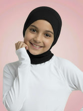 Young girl wearing a black hijab and white turtleneck against a pink background