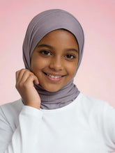 Young girl wearing a light gray hijab against a pink background