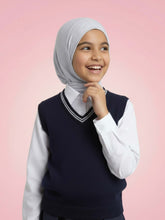 Young girl wearing a hijab, navy sweater vest, and white shirt on a pink background