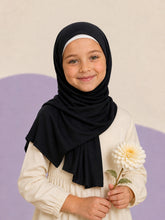 Girl wearing the black jersey hijab for girls, holding a cream dahlia, front view