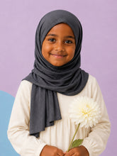 Girl wearing the charcoal jersey hijab for girls, holding a cream dahlia, front view