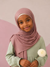 Girl wearing the dusty rose jersey hijab for girls, holding a cream dahlia, front view