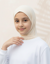 Young girl wearing a beige hijab and white top against a light background