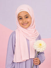 Girl wearing the pale pink jersey hijab for girls, holding a white dahlia, front view
