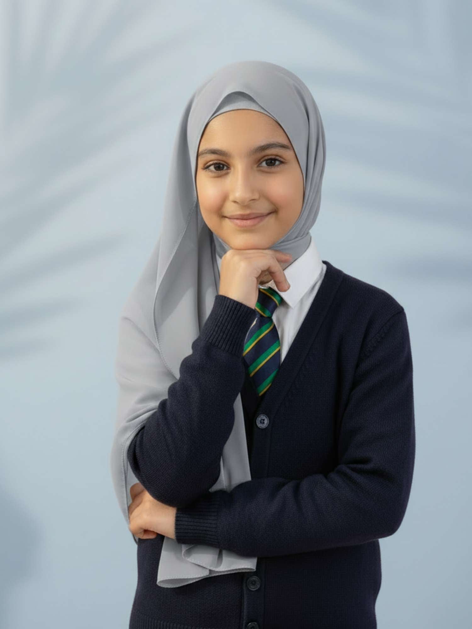 Young girl wearing a hijab, school uniform with a striped tie against a light gray background
