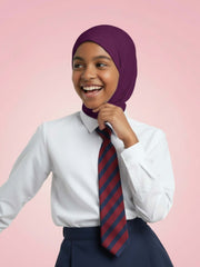 Person wearing a white shirt, navy skirt, and a striped tie with a purple hijab on a pink background