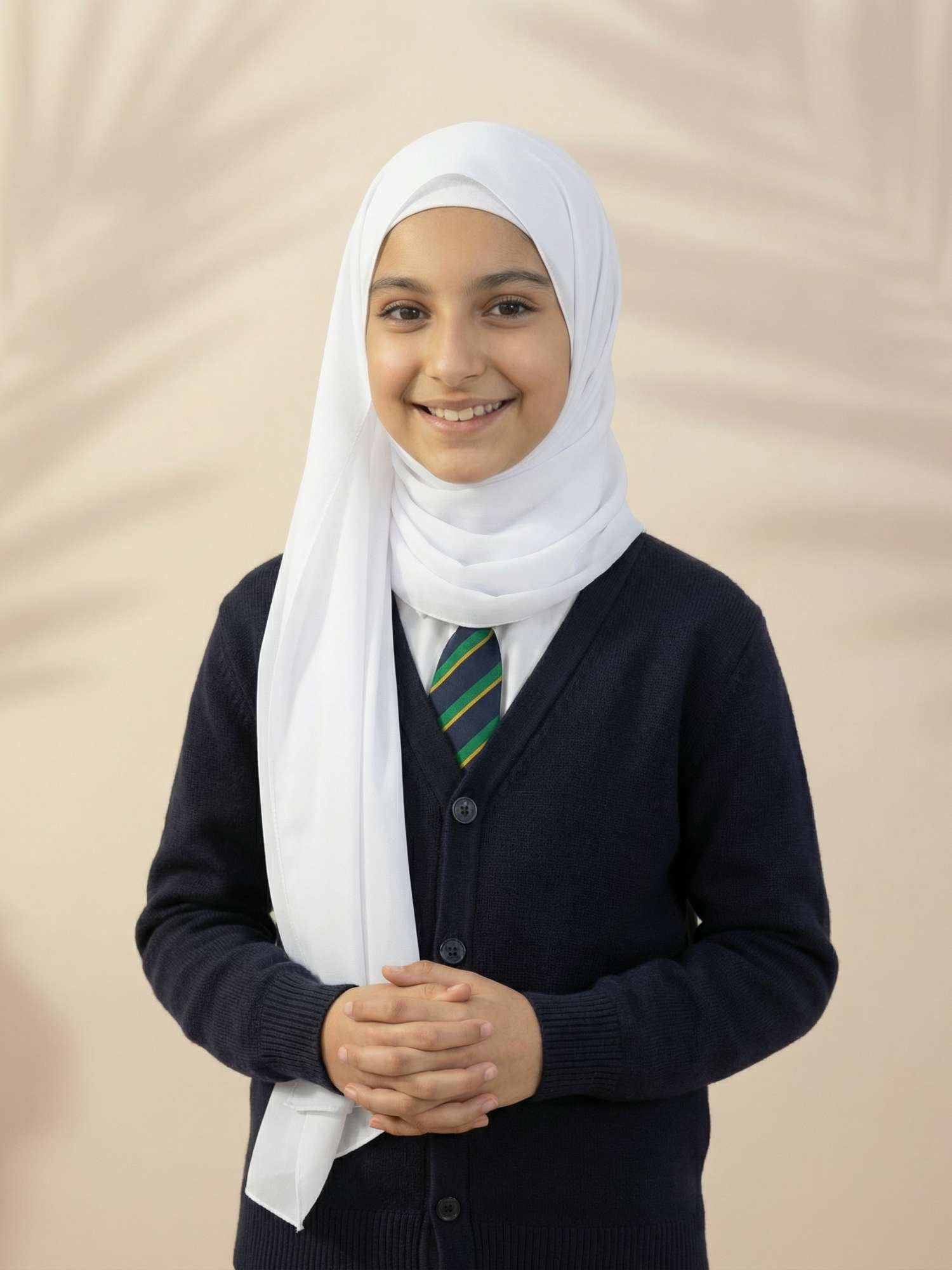Person wearing a white hijab, dark sweater, and striped tie against a beige background