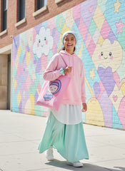 cute girl wearing a pink hoodie and light blue pants holding a pink tote bag in front of a colorful mural. Bubble Girl hijab