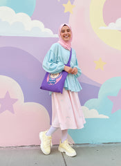 Bubble Girl hijab, girl  wearing a light blue top and pink skirt with a purple tote bag against a colorful cloud and star background.