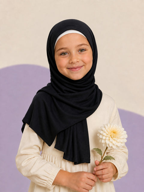 Girl wearing the black jersey hijab for girls, holding a cream dahlia, front view