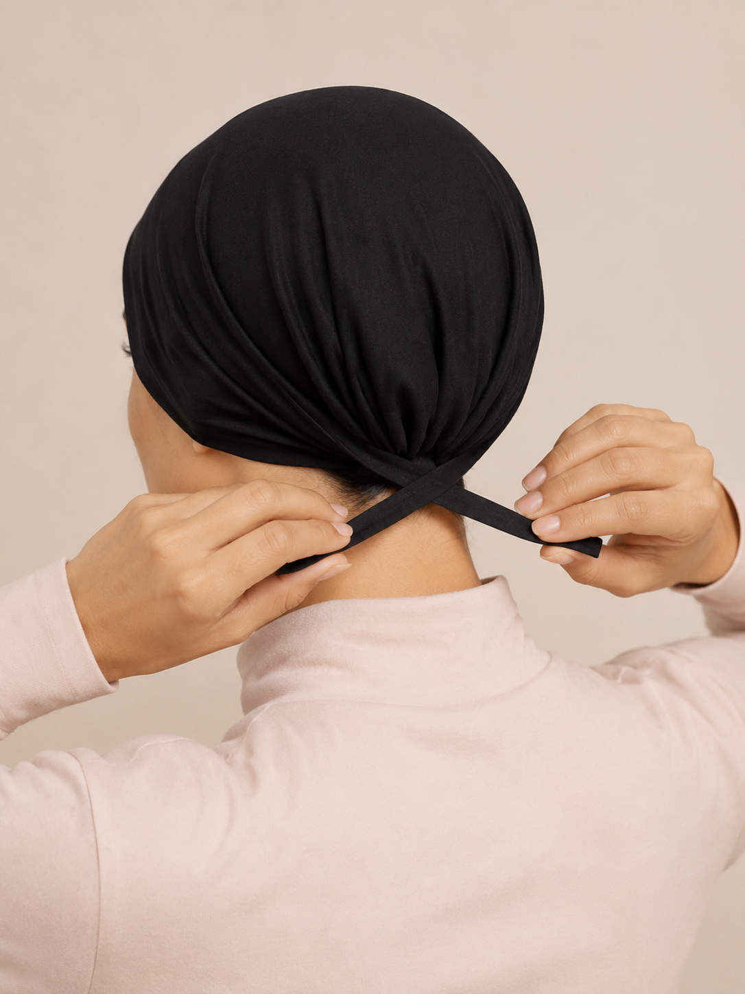 Black jersey tie-back undercap worn under a hijab, back view showing the fabric ties fastened at the nape