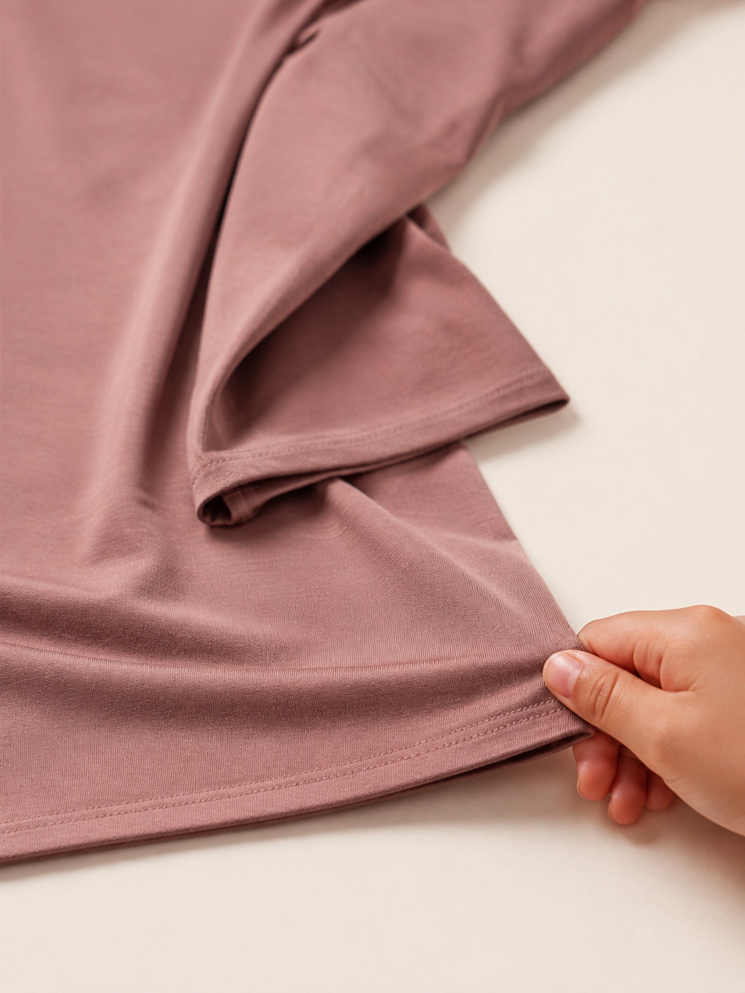 Close up of a hand drawing the dusty rose jersey hijab fabric across a pale surface