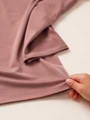 Close up of a hand drawing the dusty rose jersey hijab fabric across a pale surface