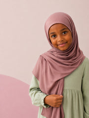Girl wearing the dusty rose jersey hijab for girls on a plain backdrop, front view