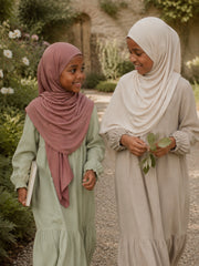 Two girls walking through a garden, one in the dusty rose jersey hijab and one in cream