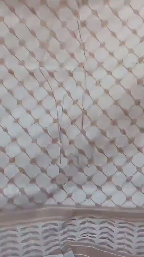 A cream keffiyeh unfolded by hand.