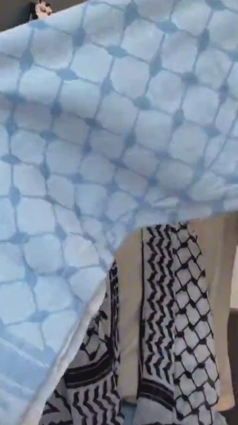 A pale blue keffiyeh held up to show the woven pattern.