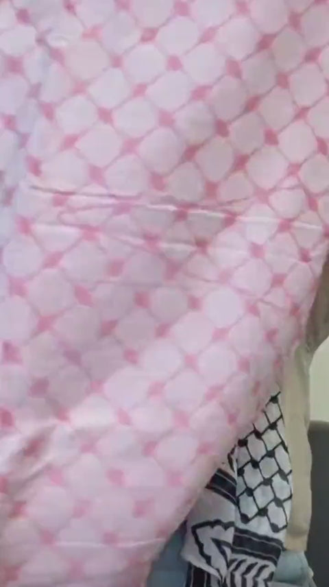 A pink keffiyeh held up to show the woven pattern.