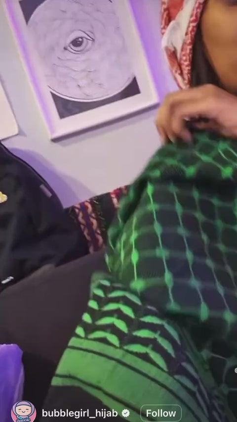 A green cotton keffiyeh worn over the shoulder.
