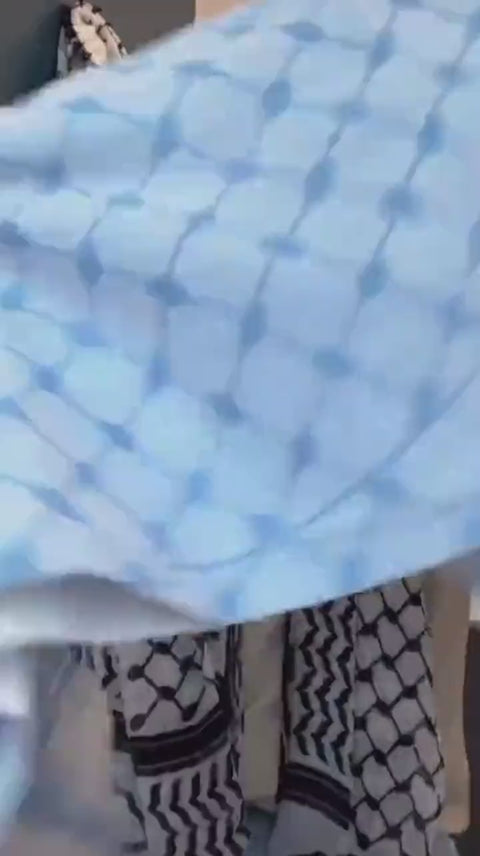 A pale blue cotton keffiyeh shaken out and draped by hand.
