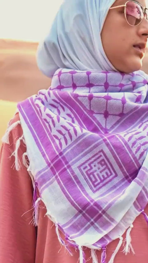 A lilac and white cotton keffiyeh at the shoulders, showing the woven square and the fringe.