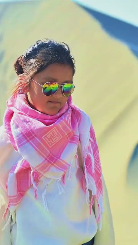 A pink and white cotton keffiyeh worn outdoors in sunlight.