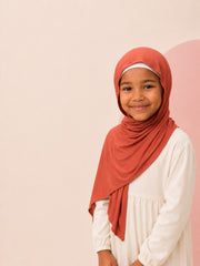 Girl wearing the rust jersey hijab for girls on a plain backdrop, front view