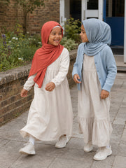 Two girls walking an outdoor path, one in the rust jersey hijab and one in light blue